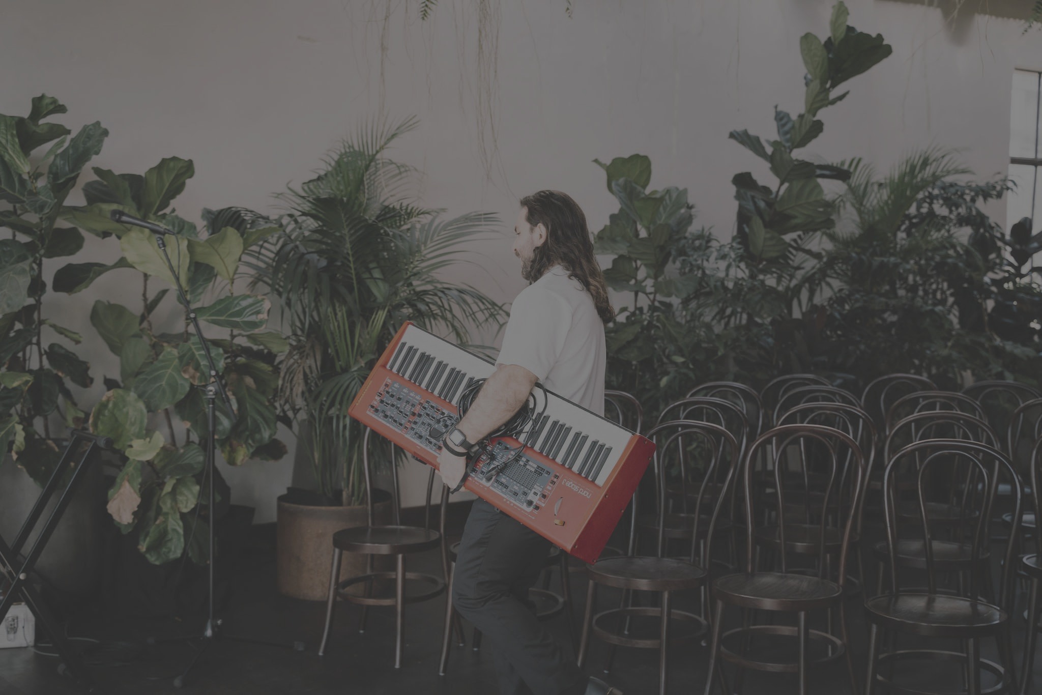 Alex Weybury carrying his keyboard into a leafy event venue